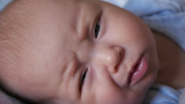 Cute baby girl opens eyes waking up after daytime sleep. Portrait of newborn kid with plump cheeks feeling sleepy in bed at home extreme closeup