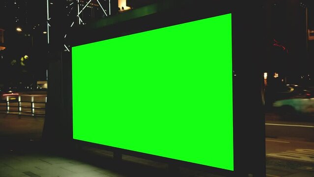 Night city large billboard with a green screen for advertising on building wall.