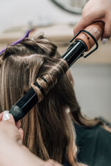 Female hands of a hair master. Close-up of blond hair on a curling iron. Curling curls.