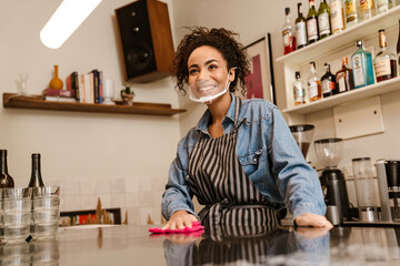 Black barista woman wearing face mask smiling while working in cafe