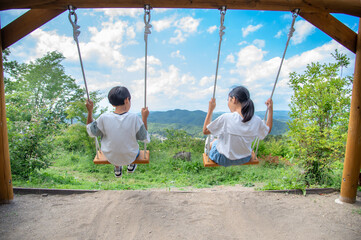山の頂上にある木製のブランコで遊ぶアジア人の小学生