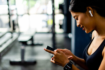 Asian woman in the gym and playing on the phone while listening to music before exercising in the...