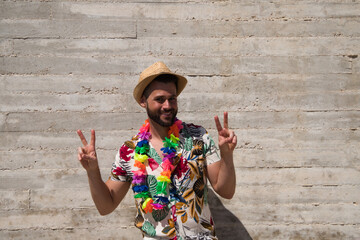 Handsome young man wearing a shirt with Hawaiian flowers, a hat and a necklace with coloured flowers. The man makes different gestures with his face and body expressions. Background grey wall.