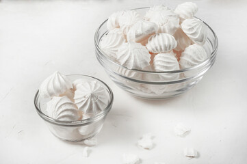 two glass vases of different sizes with French meringue dessert on a gray background, broken pieces of meringue lie next to each other.