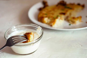on fork is piece of potato tortilla - Swiss dish, fork is raised over saucepan with cream sauce. in background, you can see part of a plate with a potato pancake, side view, natural light source.