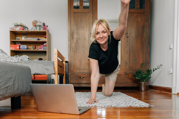 mature woman at home doing sport yoga on the floor with laptop online classes 