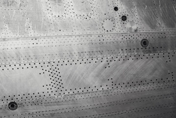 Aluminum surface of the aircraft fuselage.  Sheet metal riveted. Aircraft skin close up. Rivets on gray metal.
