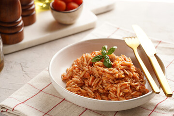 Homemade italian dish pasta risoni with tomato basil sauce in a deep bowl on checkered napkin