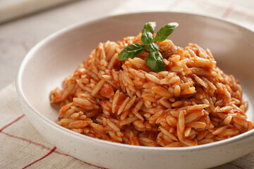 Homemade italian dish pasta risoni with tomato basil sauce in a deep bowl on checkered napkin