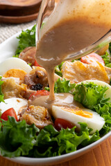 焼いた鶏肉と野菜のグリルチキンサラダに胡麻ドレッシングをかける