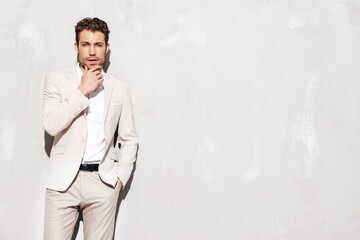 Portrait of handsome confident stylish hipster lambersexual model. Sexy modern man dressed in white elegant suit. Fashion male posing in studio near grey wall