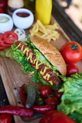 BBQ hot dog served with vegetables and French fries and sauces on wooden serving board