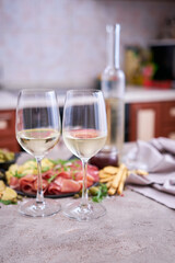 Two glasses of white wine with Italian antipasto meat platter on background