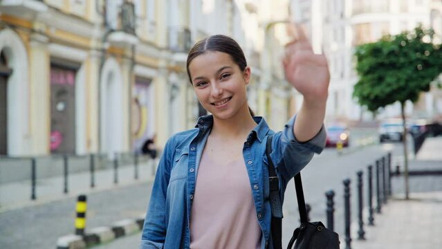 Beautiful smiling teenage girl waving hand looking at camera, outdoor