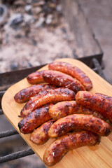 Tasty freshly grilled Sausages on charcoal grill on wooden cutting board