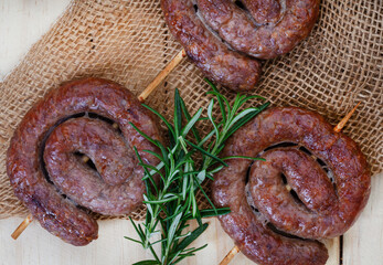  South African boerewors kebab or sosaties, perfect for the braai. Flat lay on rustic wood with burlap and fresh rosemary garnish