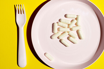 A plate containing white pills on a yellow background. The concept of vitamin intake. Top view