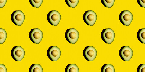 Top view of a seamless pattern of green avocados with a stone on a yellow background. Healthy summer food