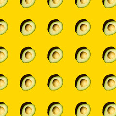 Top view of a pattern of green avocados with a stone on a yellow background. Healthy summer food