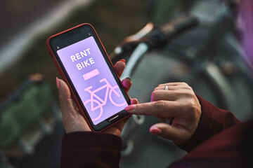 Woman renting bike using rental app on mobile phone. Using bike sharing city service. Paid rent of...