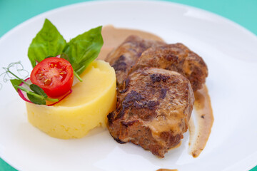 Beef cutlets meatballs with mashed potatoes on a white plate. Meat in sour cream sauce. Tomatoes and basil. Food in the restaurant. Lunch portion. Medallions.