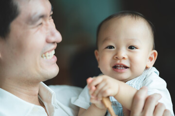 Father's Day concept, young Asian father holding a baby child with family person at home, happy childhood with love and care together, little cute son with dad and parent, parenthood lifestyle