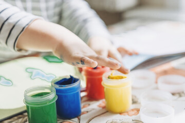 Obraz na płótnie Canvas Finger painting. Cute little boy painting with fingers at home. Close-up of child's hand in colorful paints. Early education concept. Sensory play. Development of fine motor skills.
