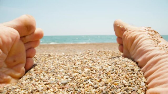 Men's feet on the sand and small stones on the beach, super macro. The sea in the background. Slow mo