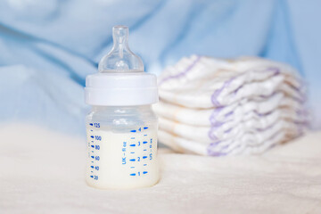 Baby bottle with milk and diapers on a white fabric background. Baby care. First days of life....