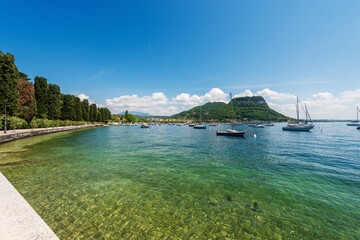 Obraz premium Beautiful bay of Lake Garda with many boats moored in front of the small town of Garda, tourist resort on the coast of Lake Garda. On the horizon the hill, Rocca di Garda. Verona, Veneto, Italy.
