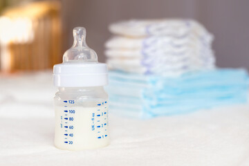 Baby bottle with milk and diapers on a white fabric background. Baby care. First days of life. Feeding and motherhood