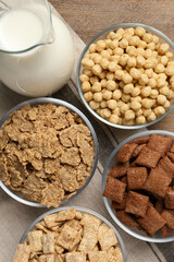 Different breakfast cereals and milk on wooden table, flat lay