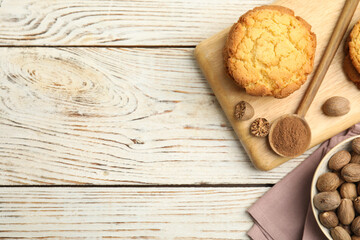 Nutmeg powder, seeds and tasty cookies on white wooden table, flat lay. Space for text