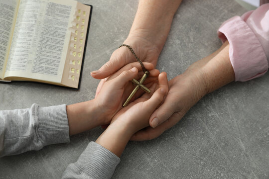 Boy and his godparent holding cross at grey table, closeup