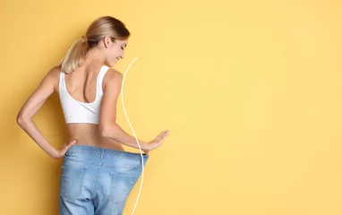 Poster Happy young woman with slim body in oversized jeans on yellow background, space for text. Weight loss © New Africa