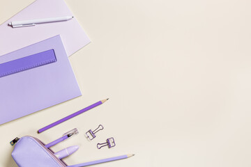 Frame with notebook violet color, pencils, pens, paper clips, pencil case, school stationery flat lay. Back to school concept on beige background, copy space. Office supplies on table