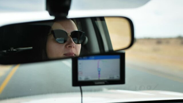 A woman - filmed through the rearview mirror - driving through the desert in Namibia.