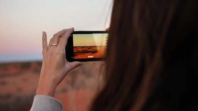 A woman is taking photos on her phone in the wide desert of Namibia. The cell phone display is filmed.