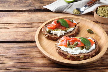 Delicious sandwiches with cream cheese, salmon, capers and pesto on wooden table. Space for text