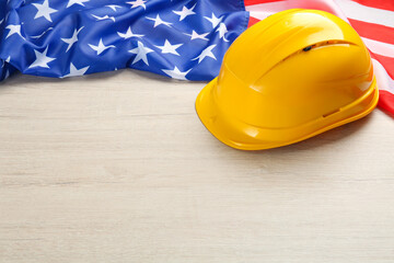 Yellow protective hard hat and American flag on white wooden table. Space for text