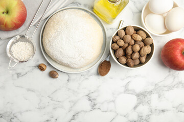 Raw dough, nutmeg seeds and other ingredients on white marble table, flat lay. Space for text