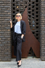 Beautiful blonde young woman wearing suit and walking on the street. A woman dressed in a business style walks around the city