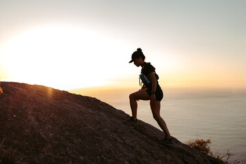 Side view of sportswoman climbing up on hill against sunset