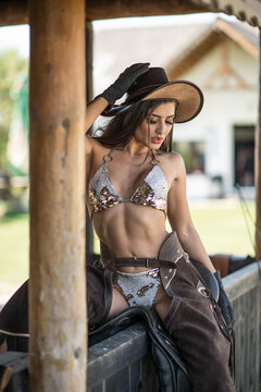 sensual brunette woman with sexy country look . Portrait of a girl with brow lingerie ,cowboy leather pants and gloves. Girl interacting and having fun at the ranch. American sexy country style