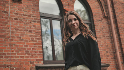 A young girl is actively posing against the backdrop of a brick building.