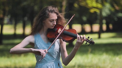 A young girl plays the violin in the city park.