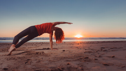 woman practicing yoga exercises while sun peeks over horizon of beach