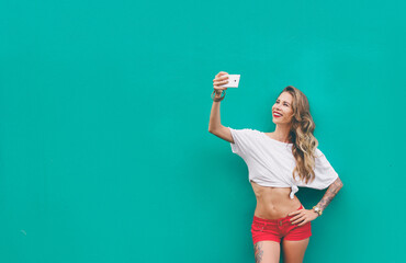 Youth and technology. Pretty sporty young woman in shorts taking selfie on smartphone. Green background.