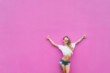 The best! Young pretty smiling woman rising hands with thumbs up against pink wall.