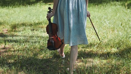 A girl in a dress walks with a violin in a city park.